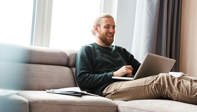 Concentrated young bearded man sitting in home using laptop computer.