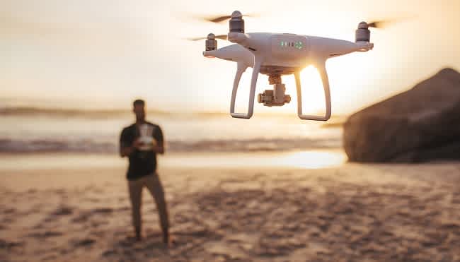 out of focus man on the beach is flying an in focus drone