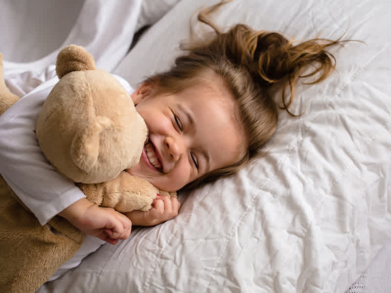 Young girl cuddling her teddy in a warm bed