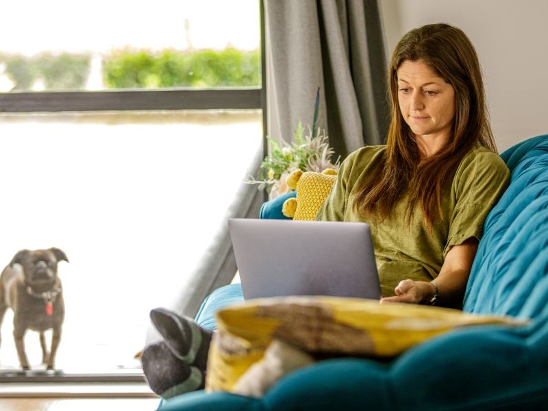 A young woman sitting on her coach, researching home insurance on her laptop