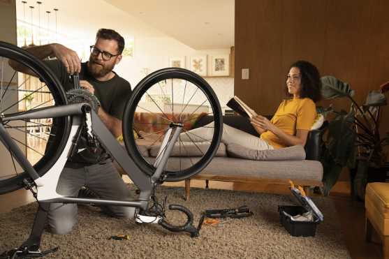 guy repairing bicycle in lounge as woman looks on from the couch.