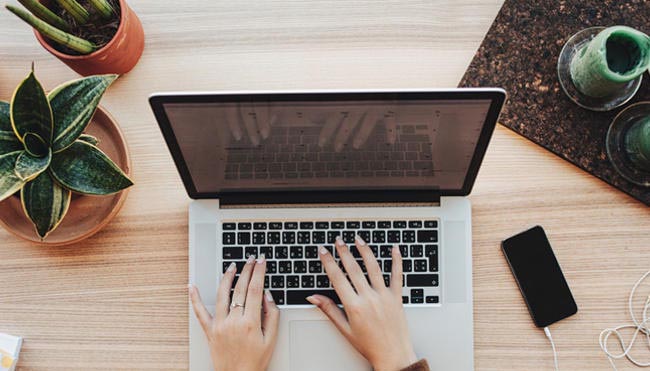 overehad shot of a laptop on a desk decorated with candles and house plants.