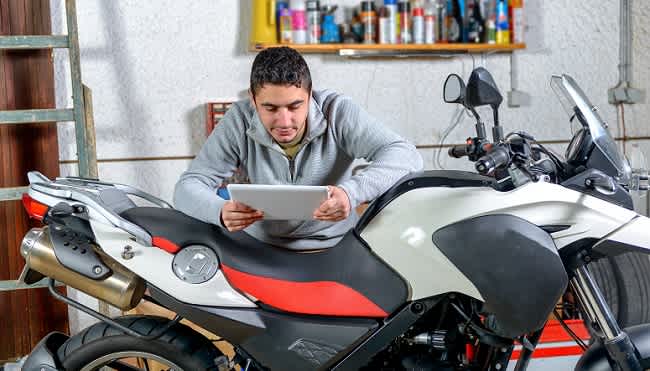 young motorcyclist reviews care tips on his tablet while working on his motorcycle in a garage