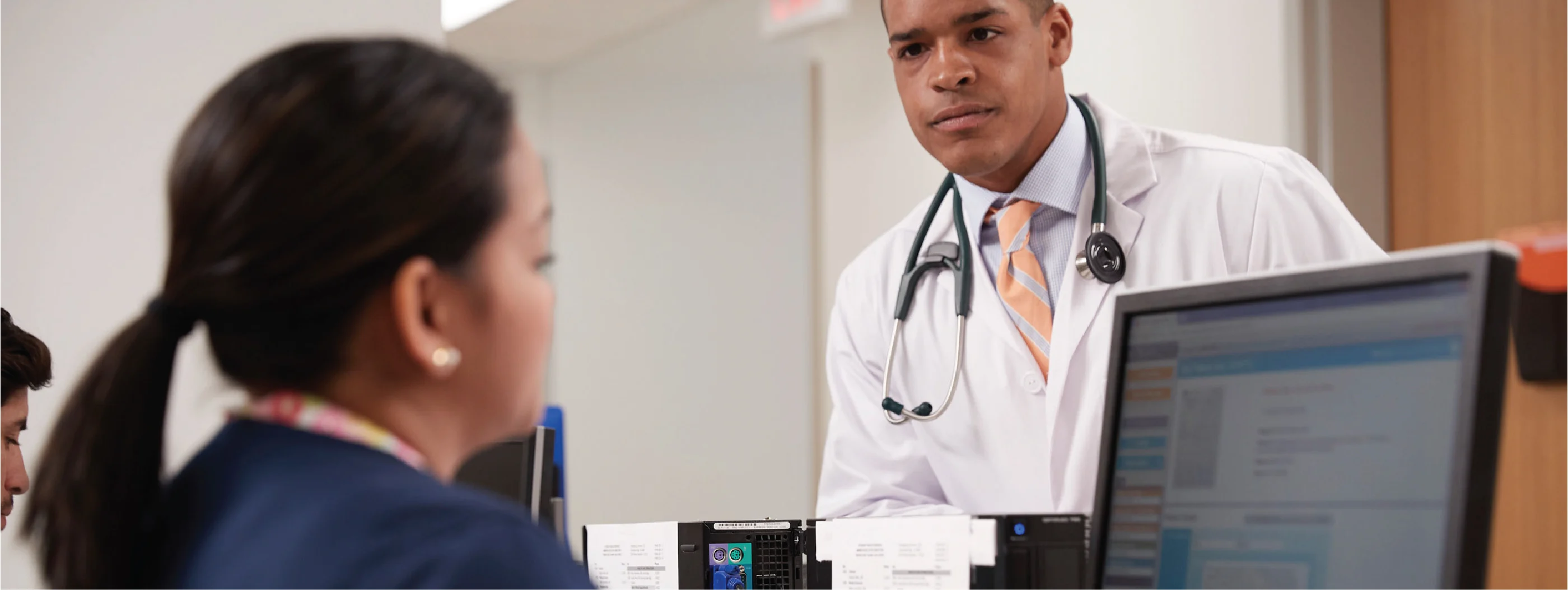 A doctor speaks with a member of his staff sitting at a computer