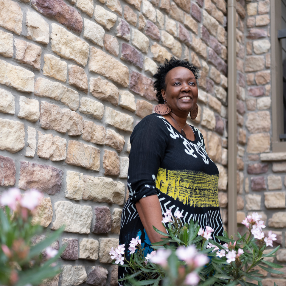 Jeannine stands against a wall outside, smiling