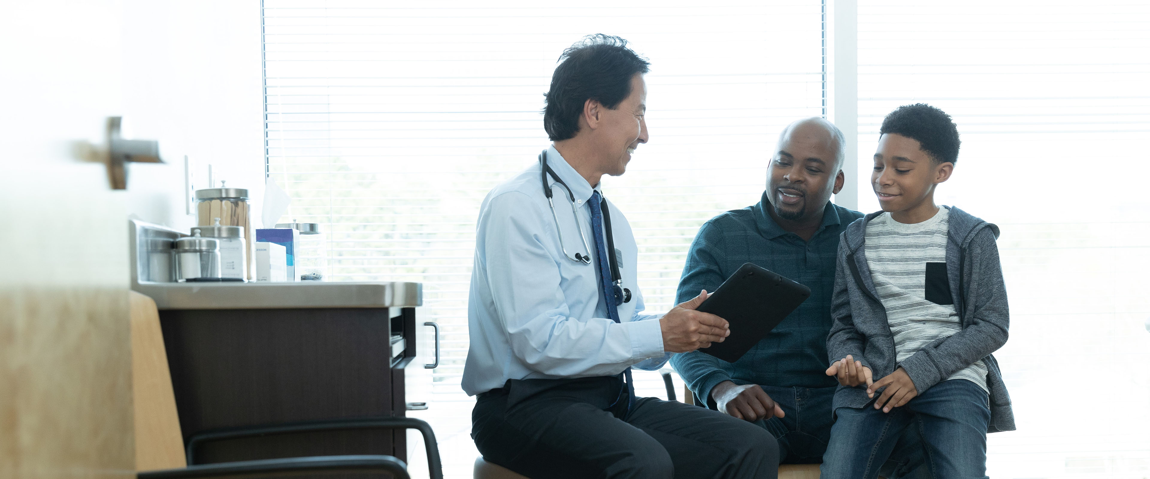 A provider discusses medication payment options with a patient and his young son.