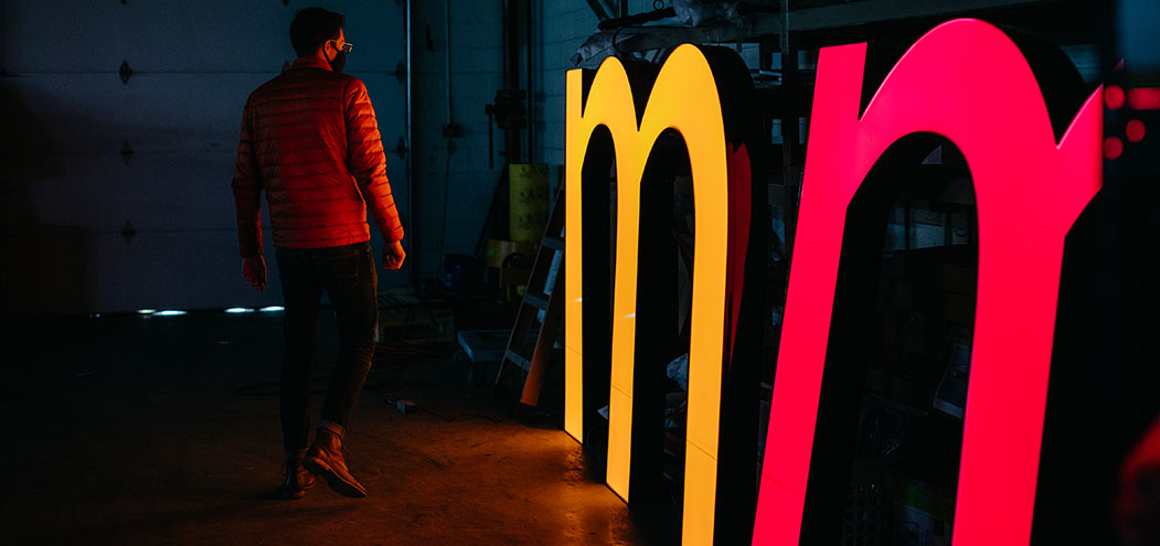 A man stands next to the gigantic letters which will form the CoverMyMeds logo sign on the exterior of our Franklinton Campus.