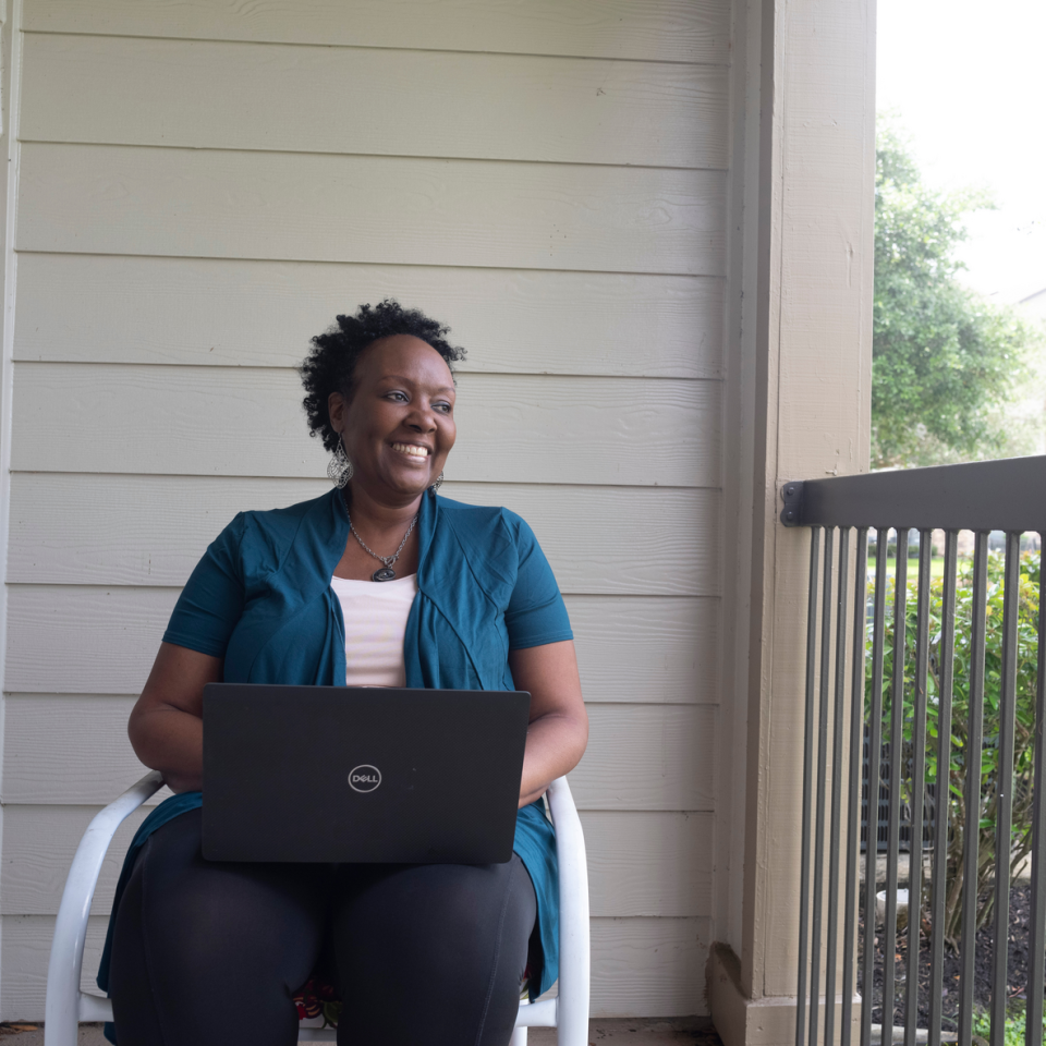 Jeannine sits outside, computer on her lap, smiling