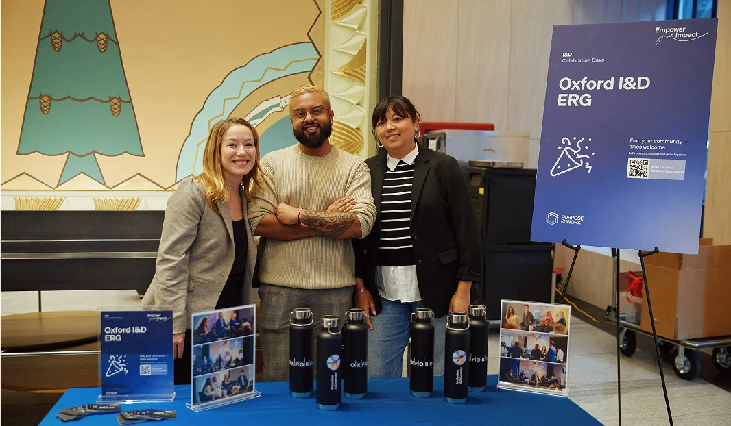 Three people standing in front of a booth for Oxford's I&D ERG