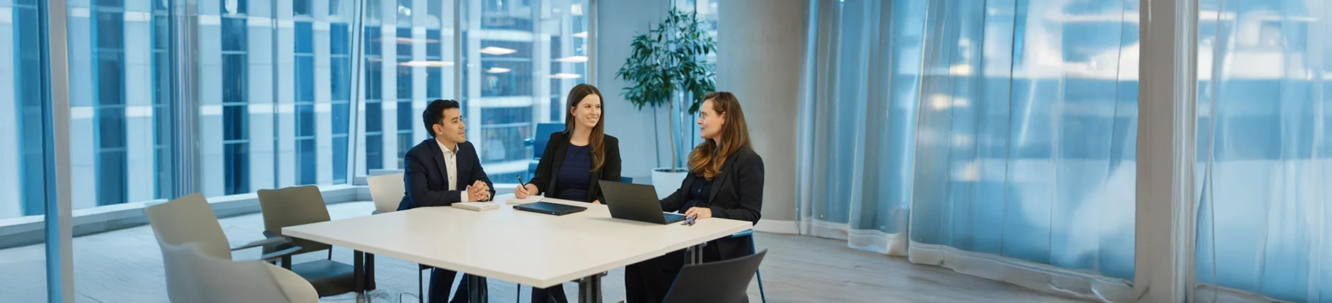 Three people sitting at a table with laptops and notebooks