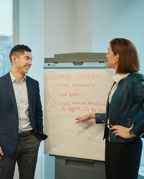 Two people standing in front of a flip chart.