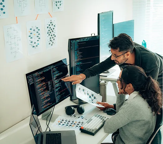Two people looking at desktop screens with code displayed