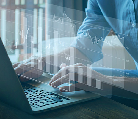 Typing on a business laptop with transparent financial charts overlaid on the image.