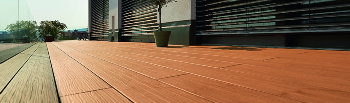 Moderne Terrasse mit Holzboden, Glasgeländer und Topfpflanzen im Freien.
