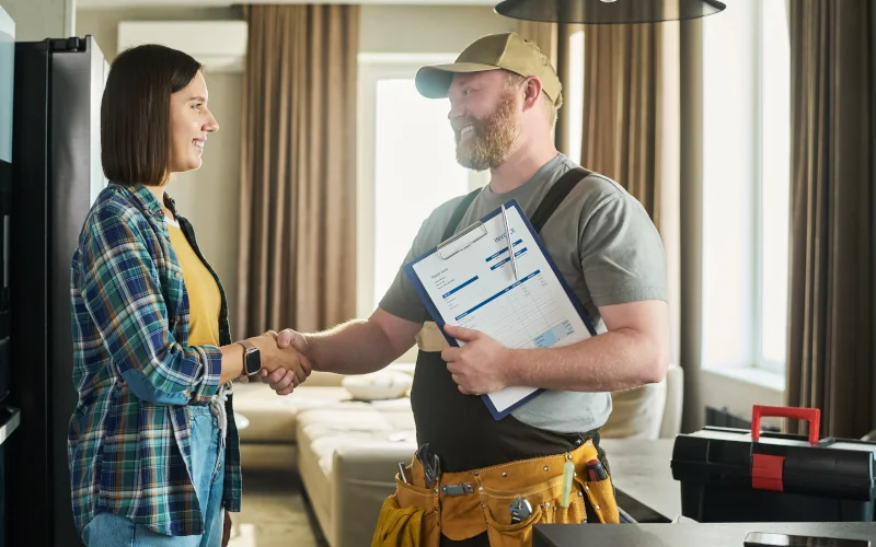 Handwerker mit Klemmbrett in der Hand schüttelt Kundin die Hand