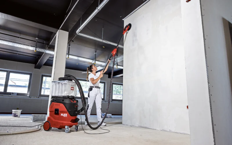 Malerin mit FLEX Wand- und Deckenschleifer in der Hand eine Wand bearbeitend