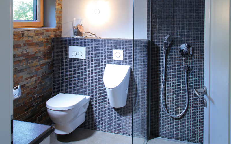 Modernes Bad mit Toilette, Urinal und Dusche mit Glasabtrennung.