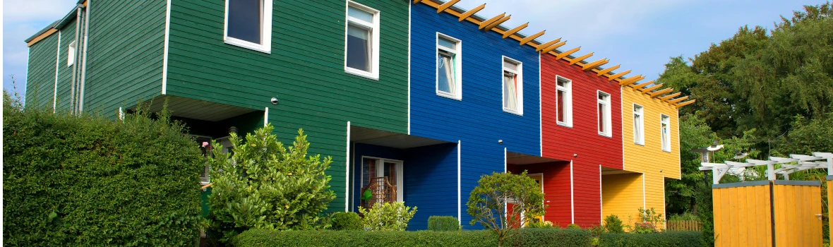 Vier zusammenhängende Reihenhäuser mit Holzfassaden. Jede Fassade hat eine andere Farbe - grün, blau, rot und grün. 