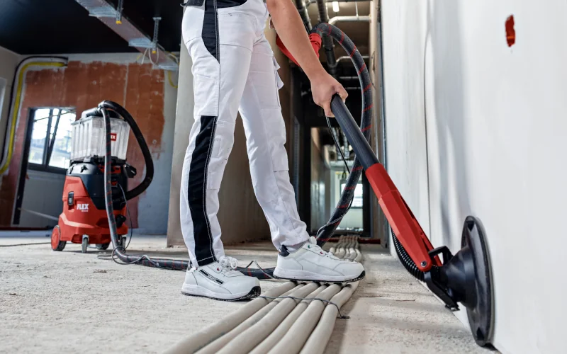 Malerin mit FLEX Wand- und Deckenschleifer in der Hand eine Wand bearbeitend