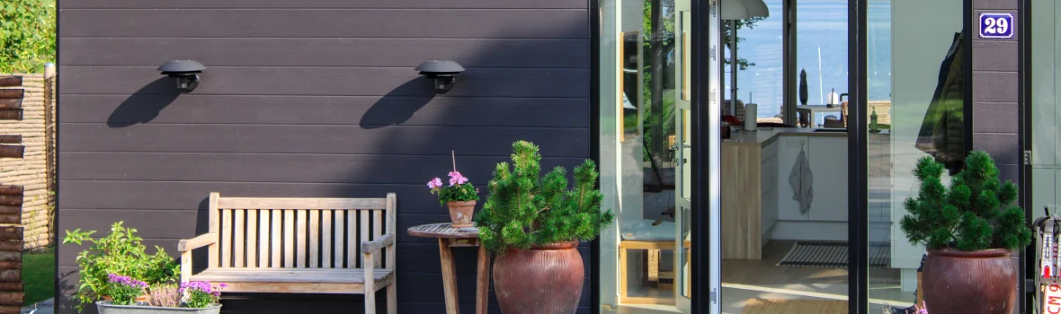 Haus mit dunklen Fassadenplatten und großer Fensterfront mit Wald im Hintergrund 
