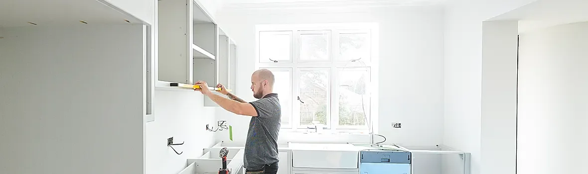 Handwerker bringt Küchenschrank an der Wand an und misst ob er gerade ist