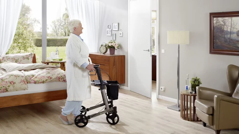 Ältere Dame schiebt am Rollator aus ihrem Schlafzimmer heraus. 