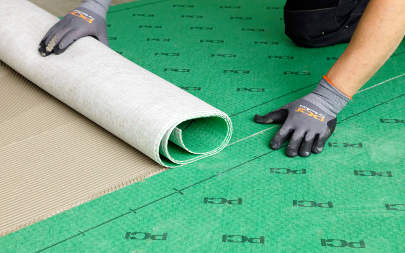 Ein Handwerker rollt PCI Fliesenuntergrund aus