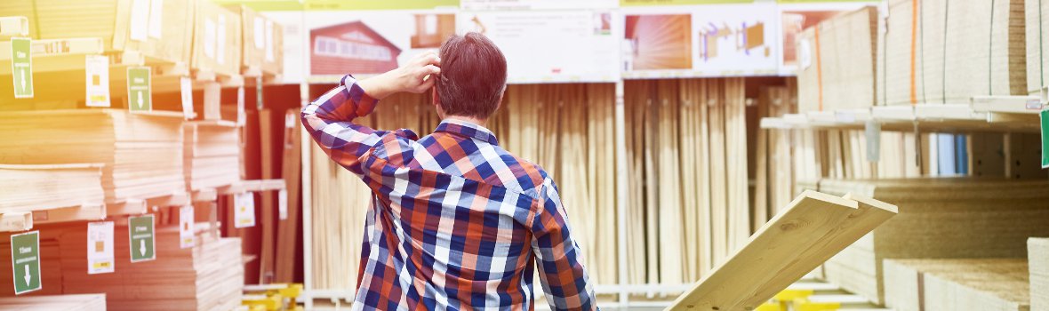 Mann steht fragend in einem Baumarkt in der Holzabteilung