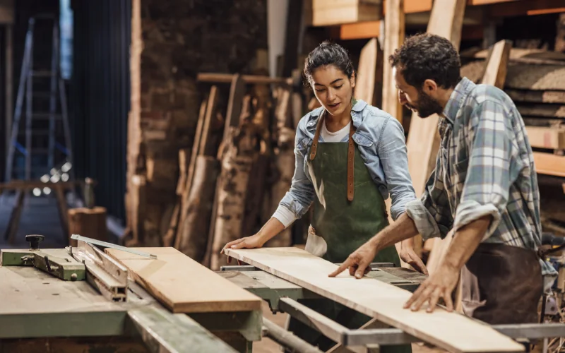 zwei Handwerker stehen in einer Werkstatt und schauen sich Holz an
