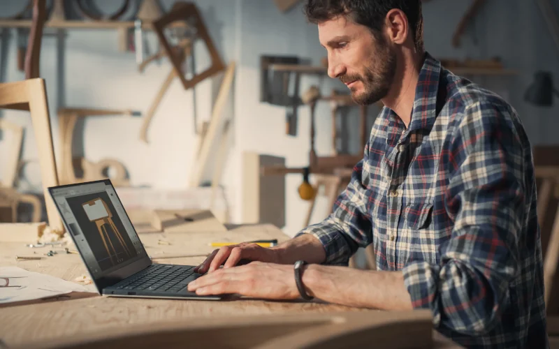 Tischler sitzt vor dem Laptop in seiner Werkstatt