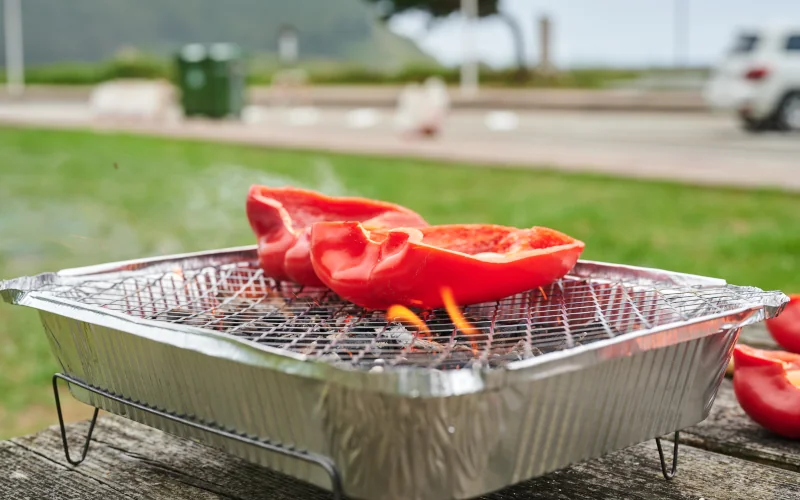 Einweggrill mit einer halbierten Paprika darauf