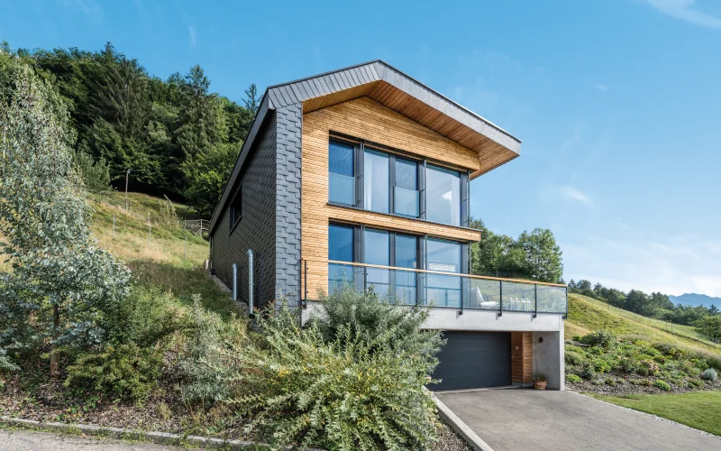 modernes Haus am Hang mit Holzfassade und Fensterfront und Garageneinfahrt 