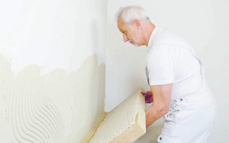Ein Mann trägt eine Dämmplatte auf eine mit Kleber bestrichene Wand auf.