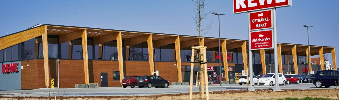 Die Frontansicht eines modernen Supermarkts in Holzbauweise mit ansprechender Holzfassade und großen Fenstern.