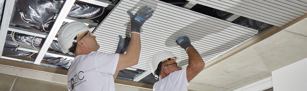 Zwei Handwerker bringen die Akustiklösung Cleaneo Stripe von Knauf an der Decke an.
