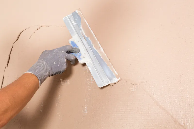 Riss in der Wand wird mit einem großem Spachtel gefüllt