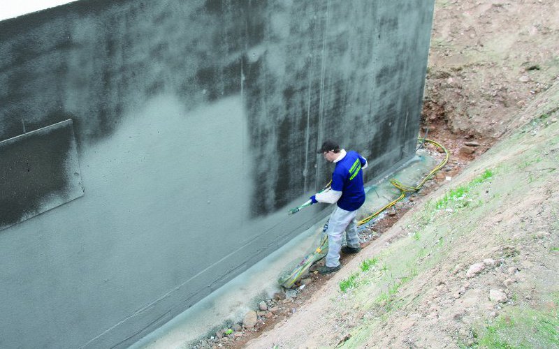 Mann besprüht eine Außenwand mit flüssigem Baustoff