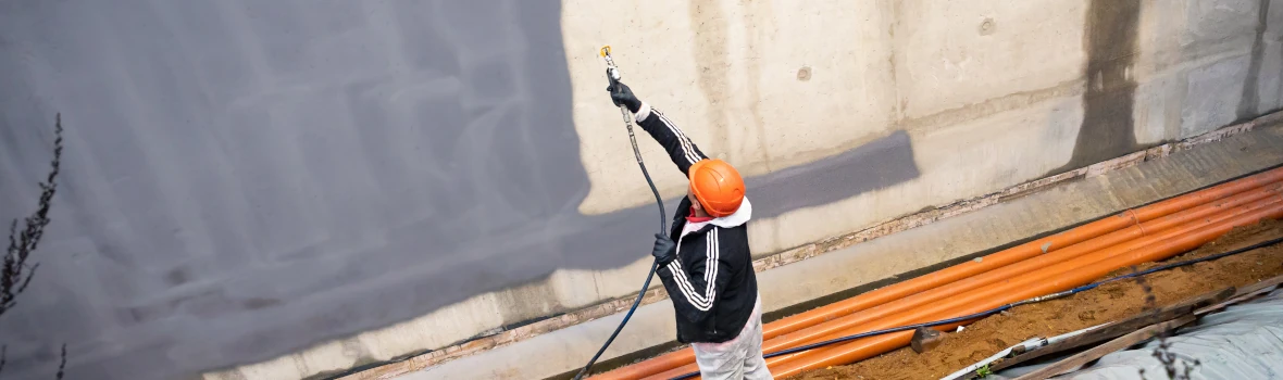 Handwerker sprüht Bauwerksabdichtungs-Masse mit einem Schlauch an die Außenwand 