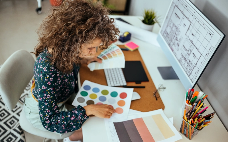 Weibliche Designerin die sich ein Farbmuster auf ihrem Bürotisch ansieht.