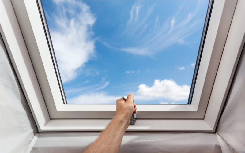 Mann öffnet ein Dachfenster mit Blick in den blauen Himmeln 