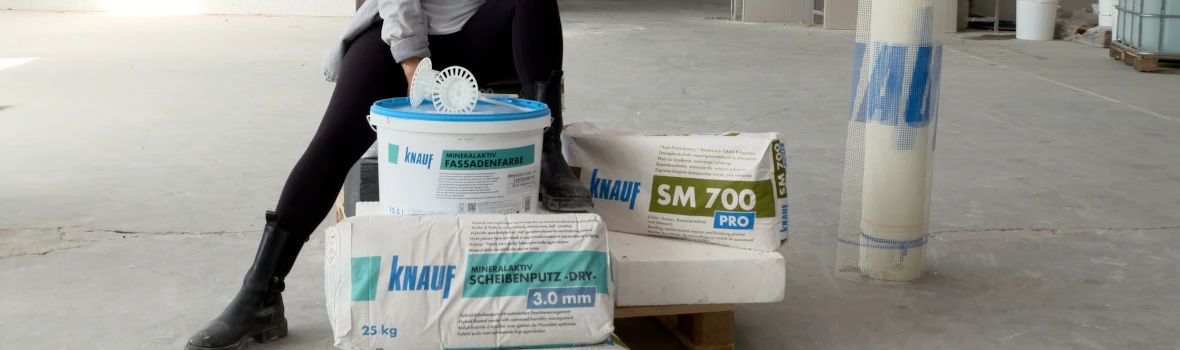 Eine Frau, die vor Produkten von Knauf sitzt. Im Hintergrund ist ein Betonboden.