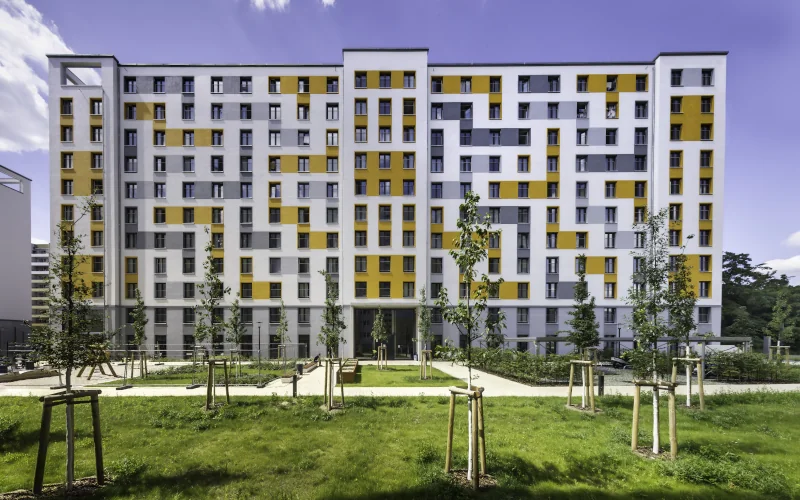 großer Wohnblock mit bunter Fassade und Begrünung davor