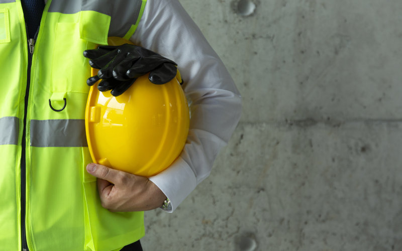 Arbeiter mit Schutzweste hält einen Bauhelm unter dem Arm 