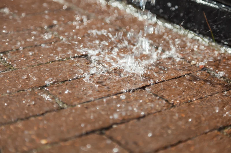 Regenwasser trifft auf Pflasterfläche, versickert teilweise durch Fugenöffnungen.