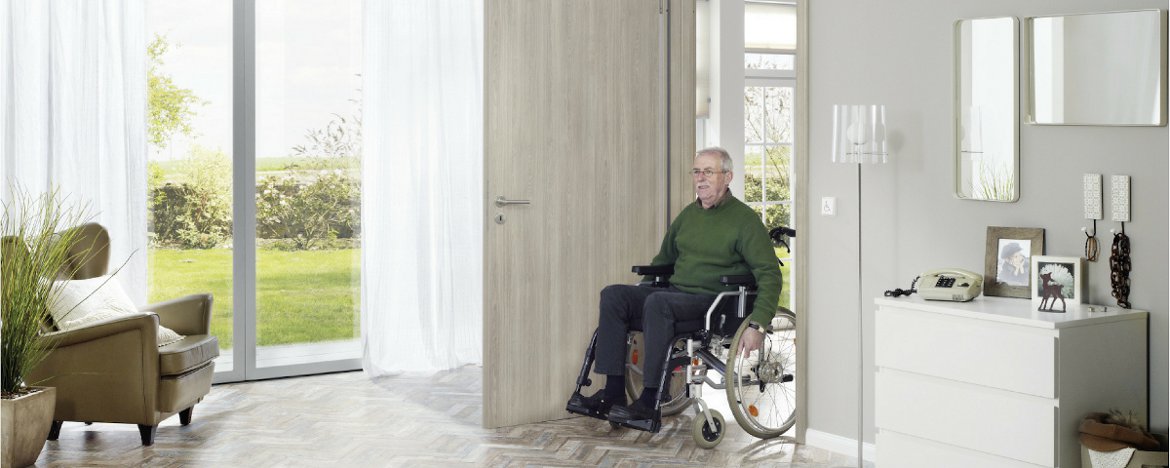 Mann rollt mit Rollator durch eine Wohnungstür. 