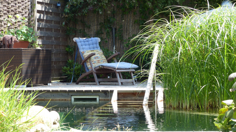 Eine Liege steht auf einer Terrasse an einem Gartenteich