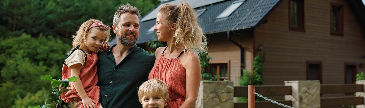 glückliche vierköpfige Familie steht vor einem Holzhaus vor einem Wald 