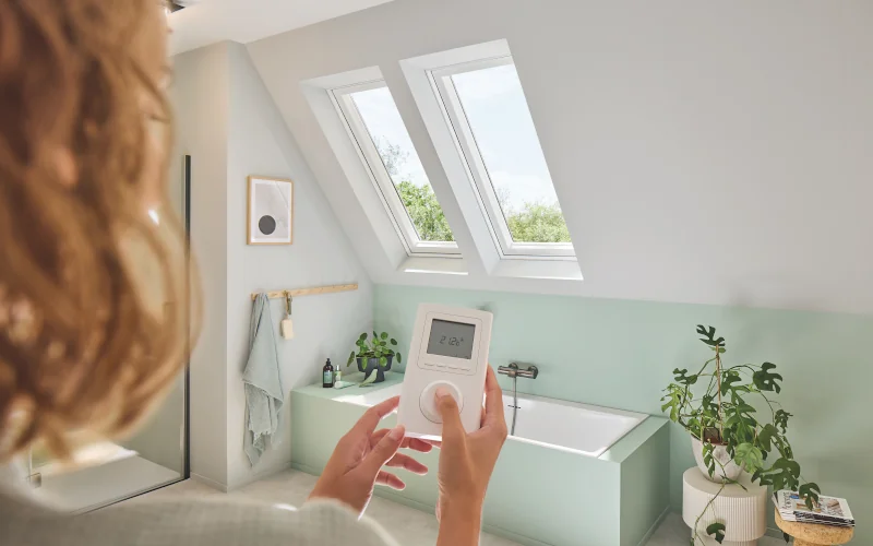 Frau mit Fernbedienung im Vordergrund, Dachfenster und Badewanne im Hintergrund