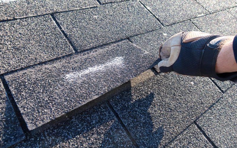 Wohnungs-Dachinspektion aufgrund eines Versicherungsanspruchs wegen Sturmschäden. Die Asphaltschindeln zeigen Anzeichen von Windschäden