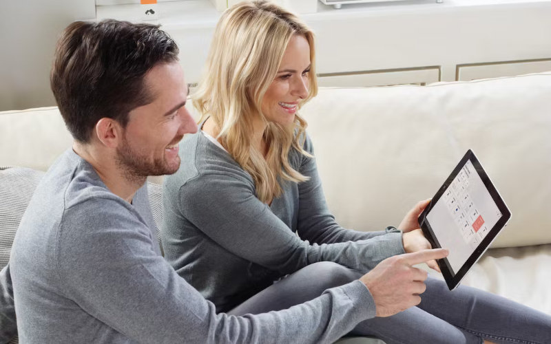 Mann und Frau sitzen auf dem Sofa und schauen ins Tablet